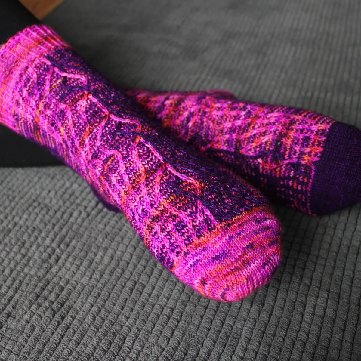 Front view of crossed legs wearing dark purple and bright pink socks with vertical stripes that create an abstract surface texture.