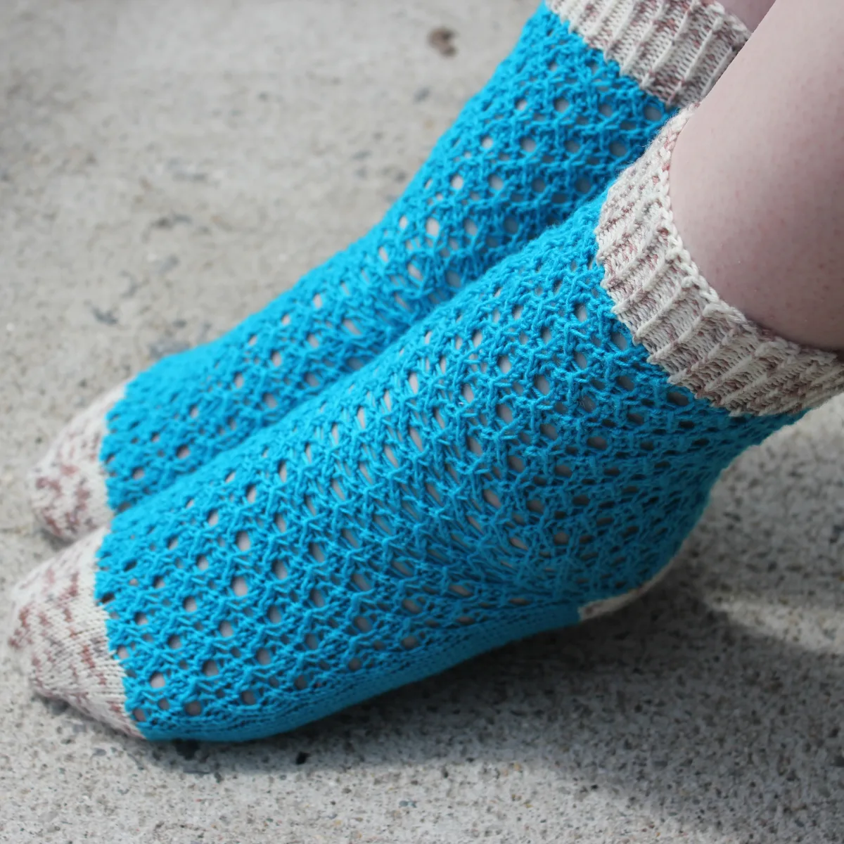 Top view of feet with pointed toes wearing bright blue lace socks with white and brown speckled heels, toes, and cuffs.