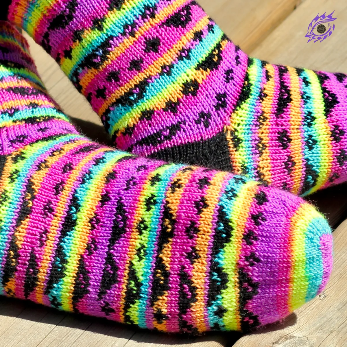 Feet wearing stranded colourwork socks with black heels and 8-bit sunglasses and sparkles motif on neon rainbow striped background.