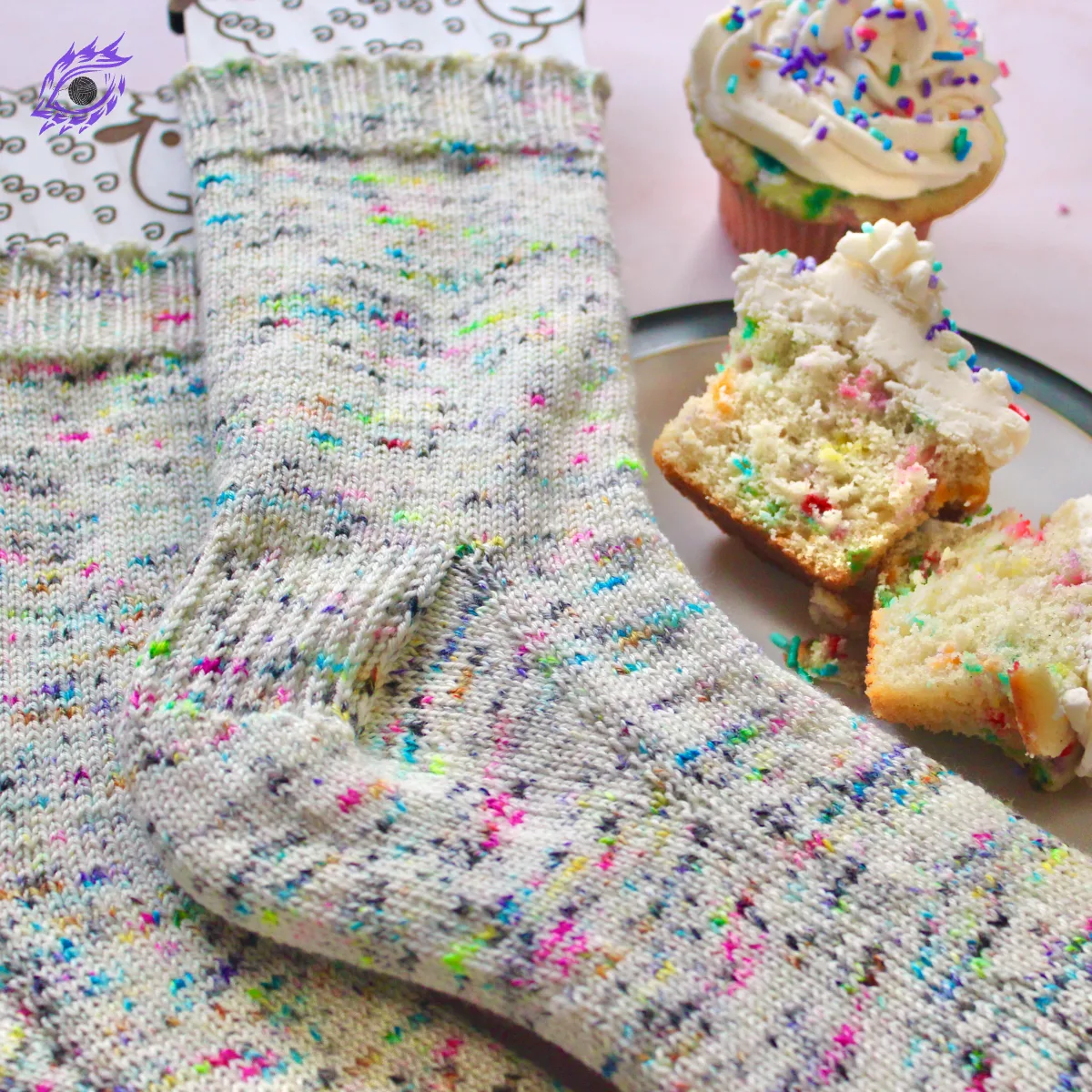 Close view of rainbow speckled socks on sock blockers beside a plate of rainbow-speckled cupcakes.