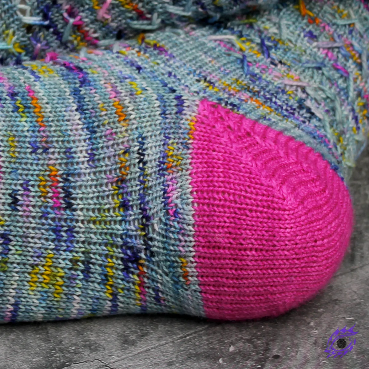 Close-up view of sole of blue sock with mini-gusset shaping beside bright pink rounded three-wedge sock heel.