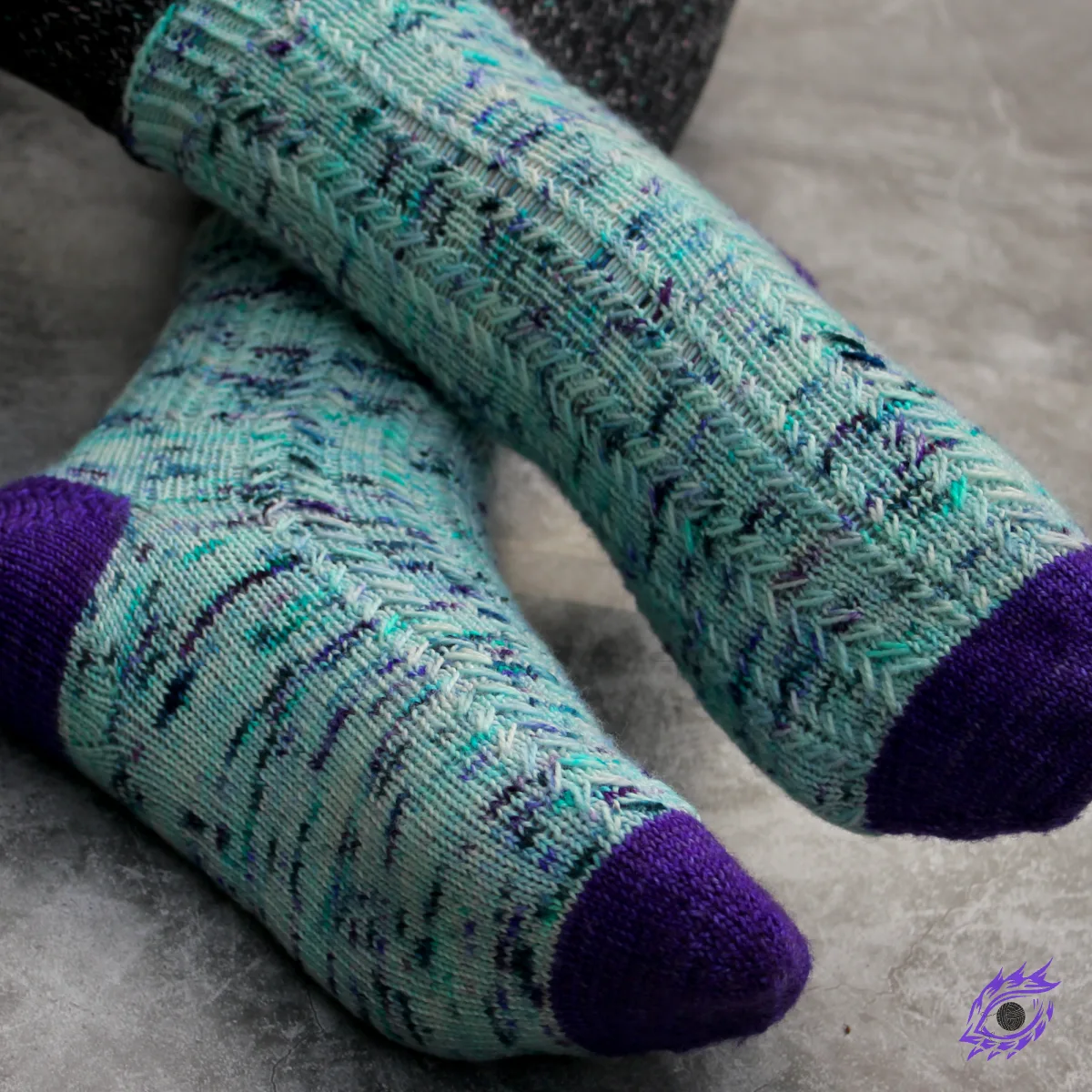 Feet wearing blue and purple knitted socks with columns of elongated-stitch cables.