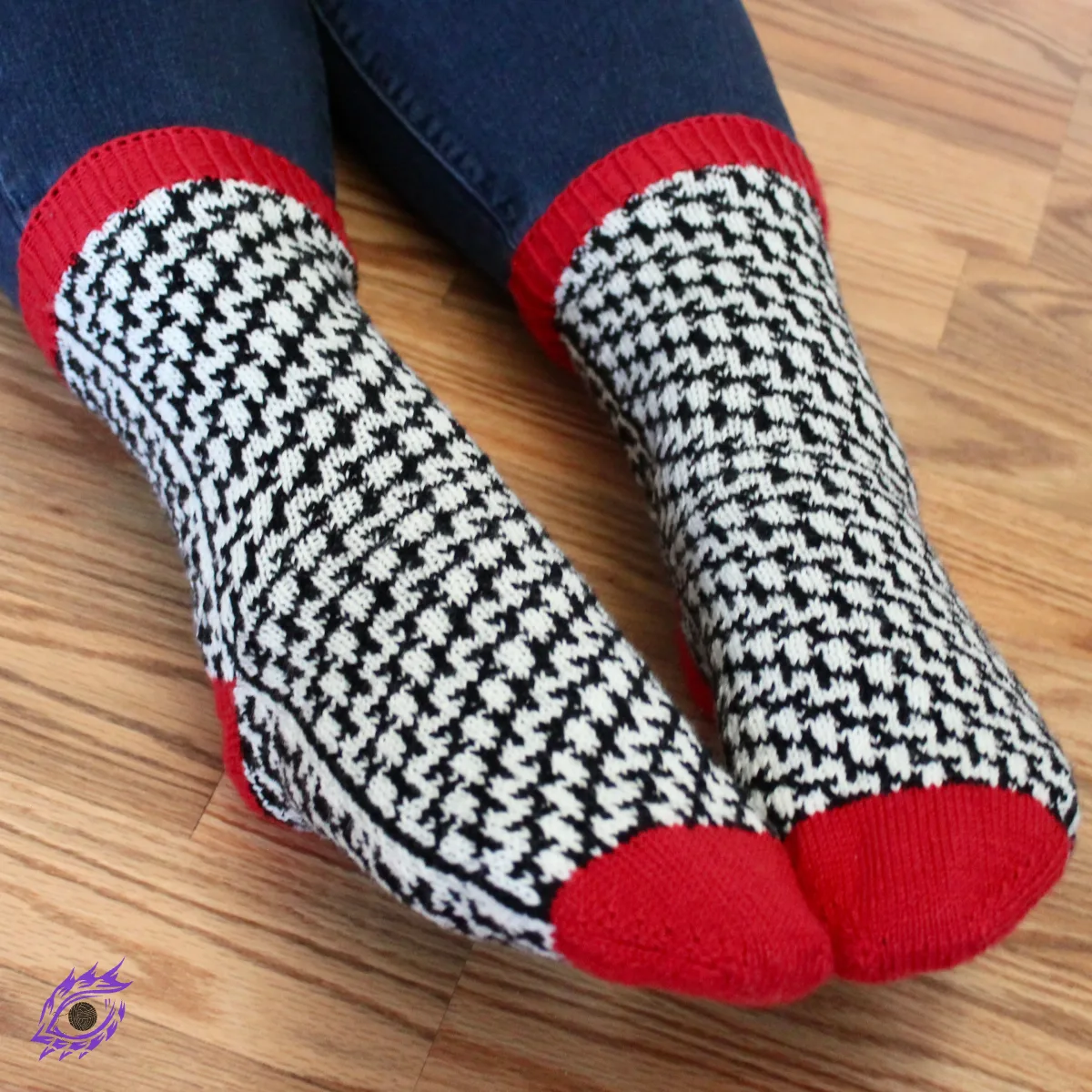 Feet wearing stranded colourwork socks with black and white mirrored optical-illusion lines and red heels, toes, and cuffs.