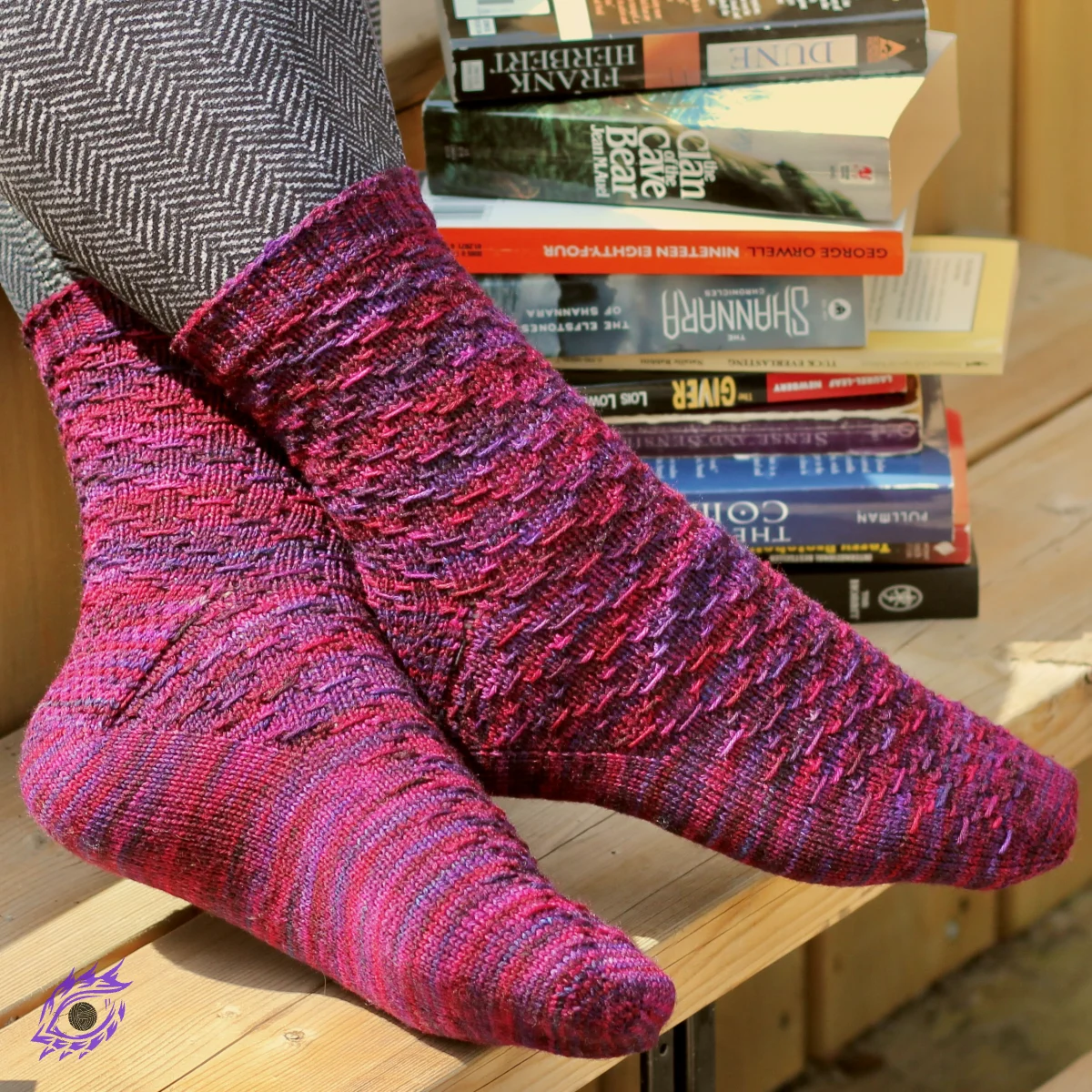 Crossed feet wearing red and purple socks with horizontal diamond-shaped surface texture with novels in the background.