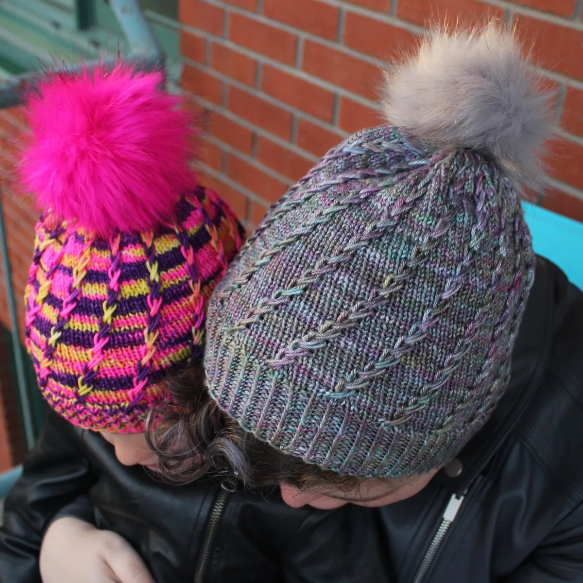 Top-down view of woman and child wearing toques with spiralling criss-crossing surface textures and coordinating pompoms.