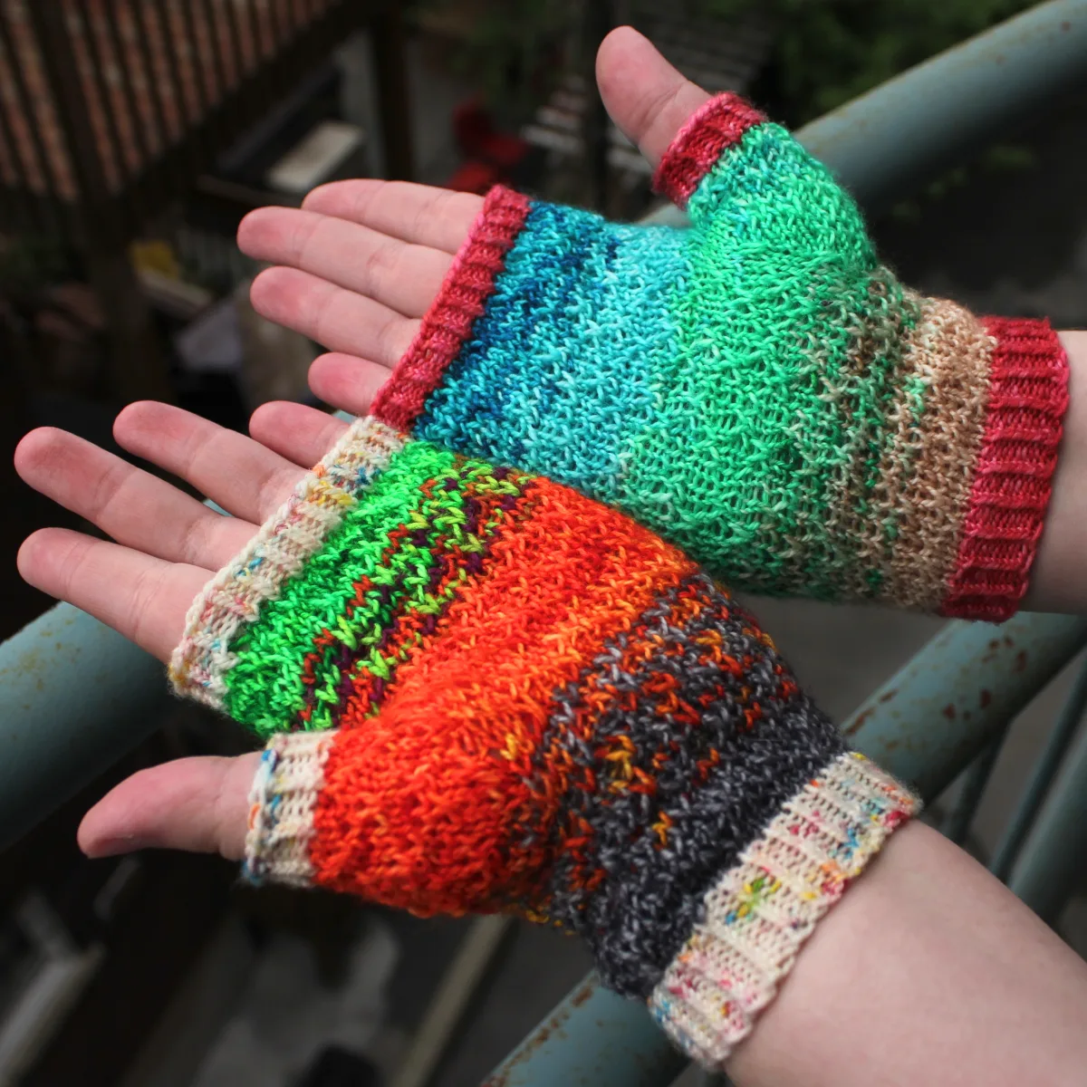 Palm-up view of mismatched multicoloured fingerless mitts with slipped-stitch texture.