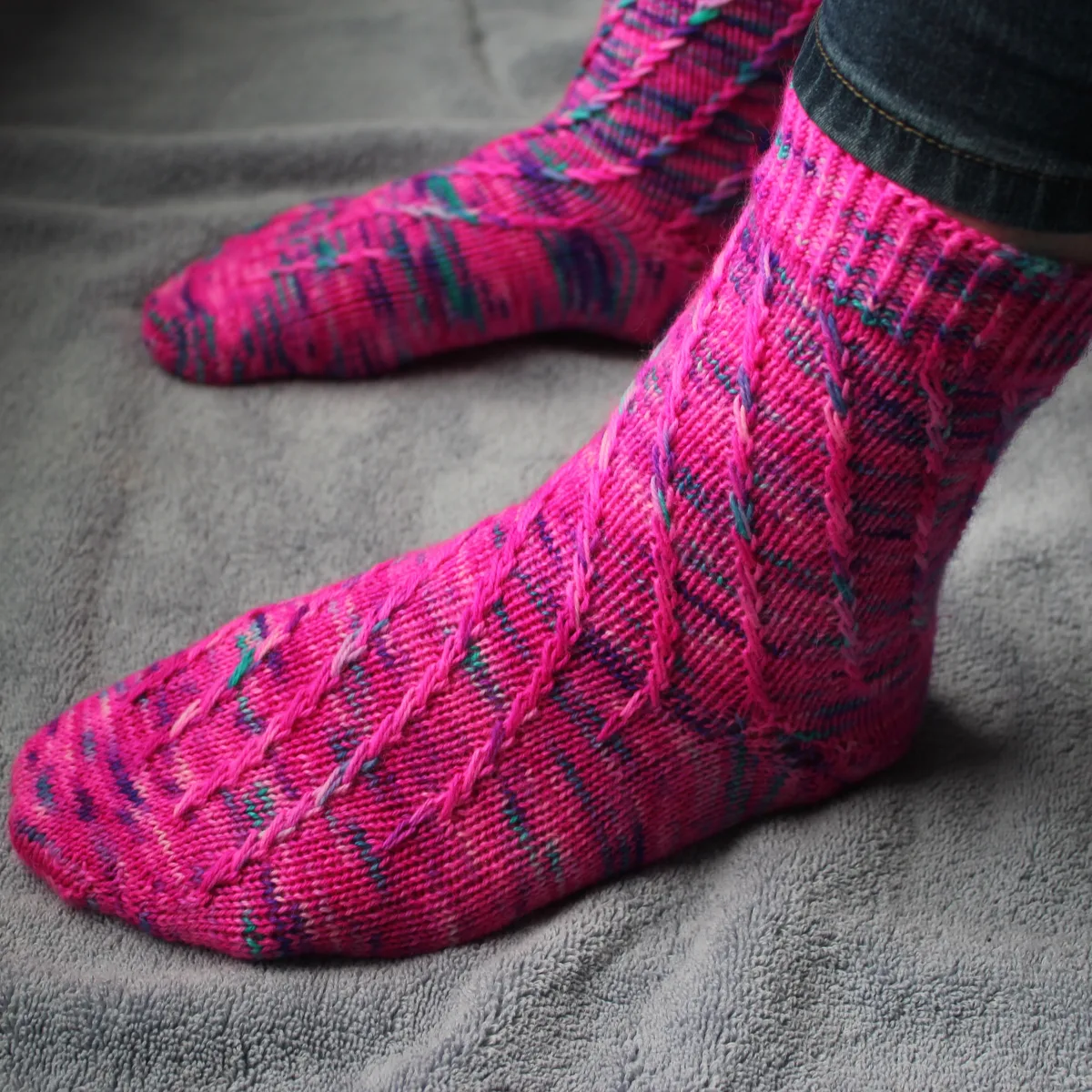 Side view of pink socks with flecks of purple and teal; they have a spiralling criss-crossing surface texture.