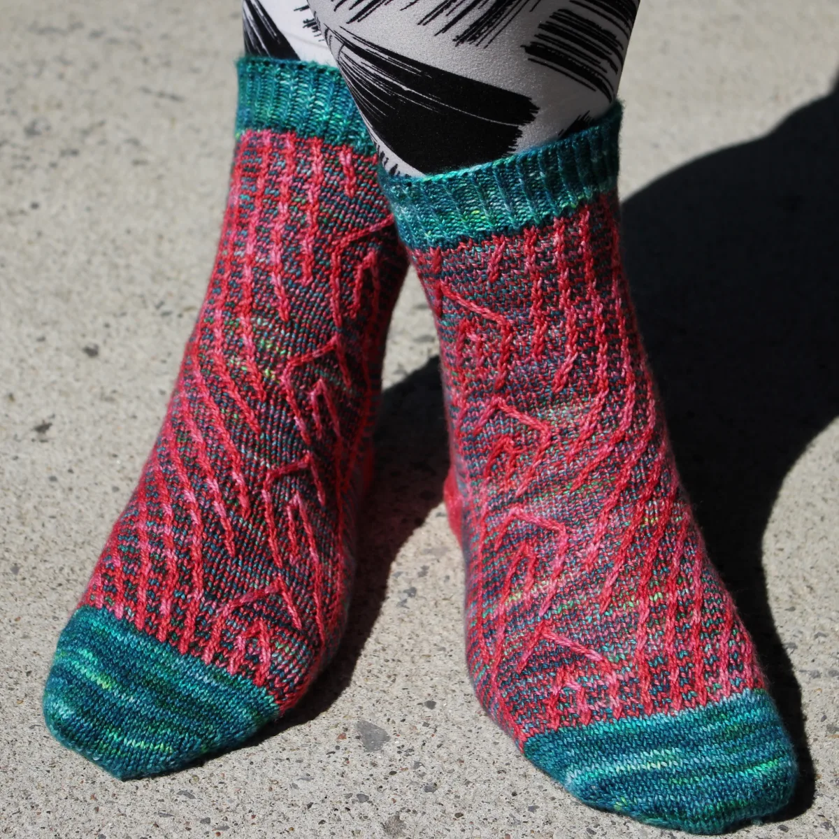 Front view of crossed legs wearing dark green and bright coral socks with vertical stripes that create an abstract surface texture.