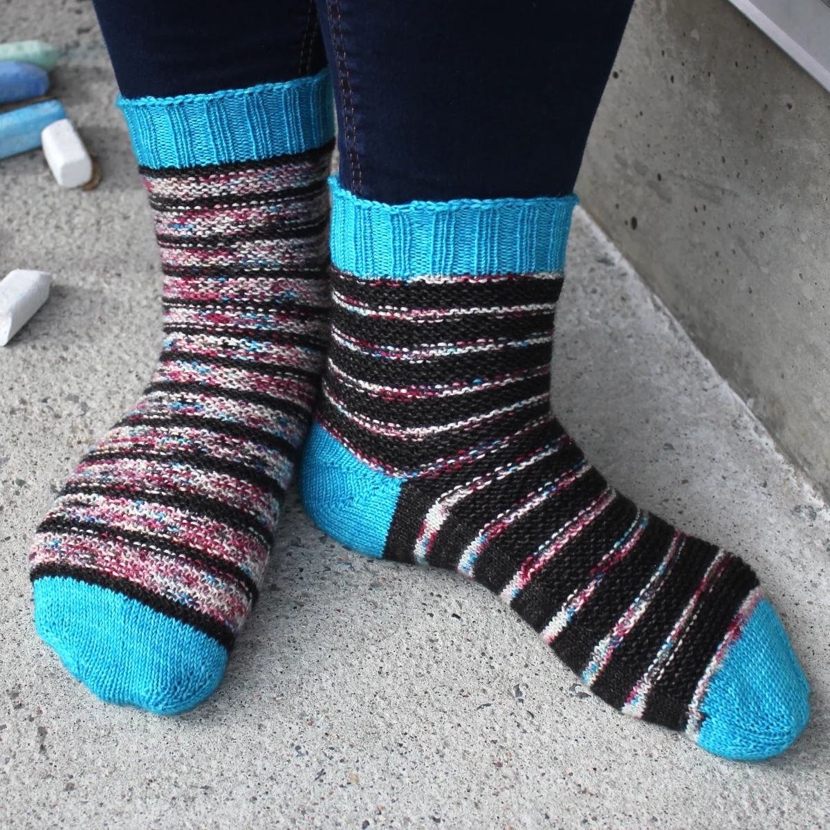 Front and side view of black and subtly-multicoloured striped socks with bumpy surface texture and bright blue heels, toes, and cuffs.