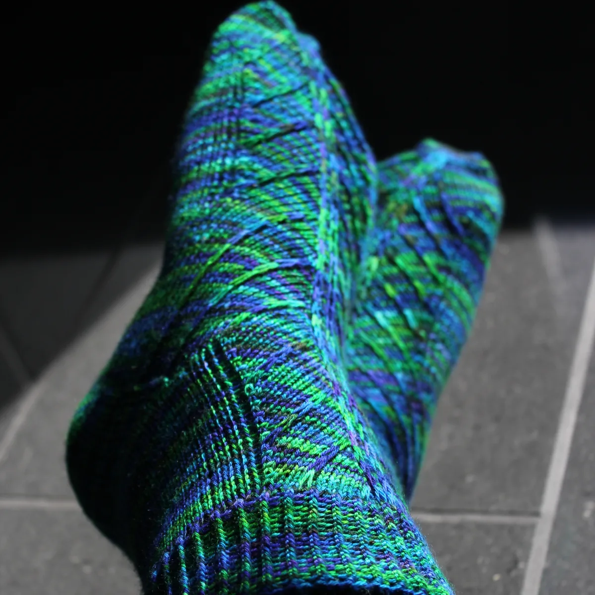 Crossed feet wearing blue-green socks with angled surface detail.