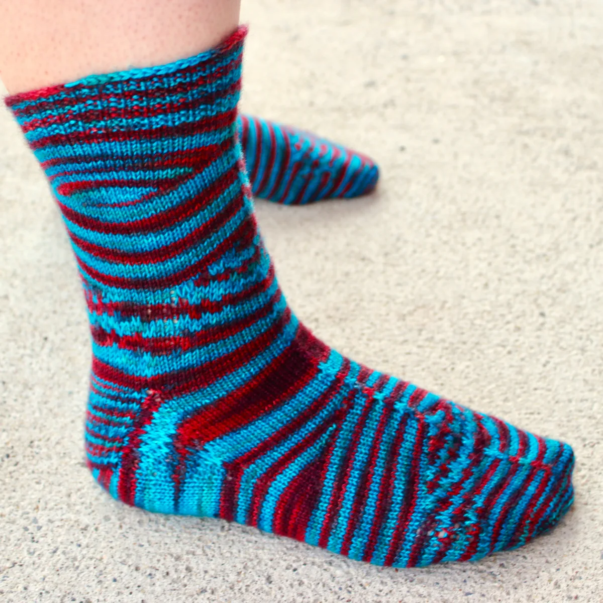 Side view of blue and red socks with shifting and pooling colour patterns and subtle surface texture.