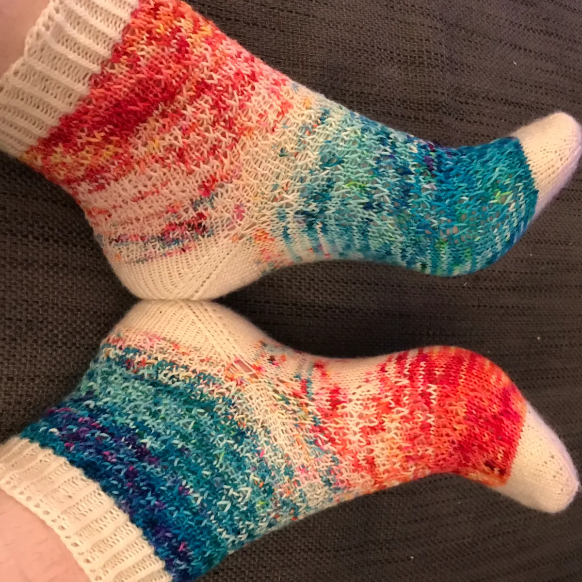 Side view of feet touching heel-to-heel wearing socks that fade from blue through white to red with white heels, toes, and cuffs.