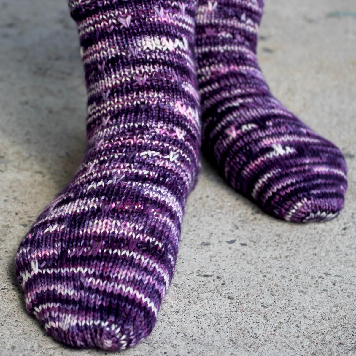 Feet wearing dark purple, pink, and white socks with slipped-stitch texture.