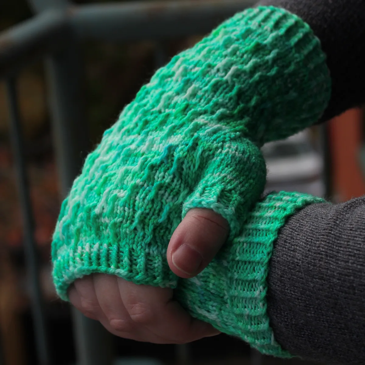 Side view of hands draped over each other wearing bright green fingerless mitts with twisted surface detail.