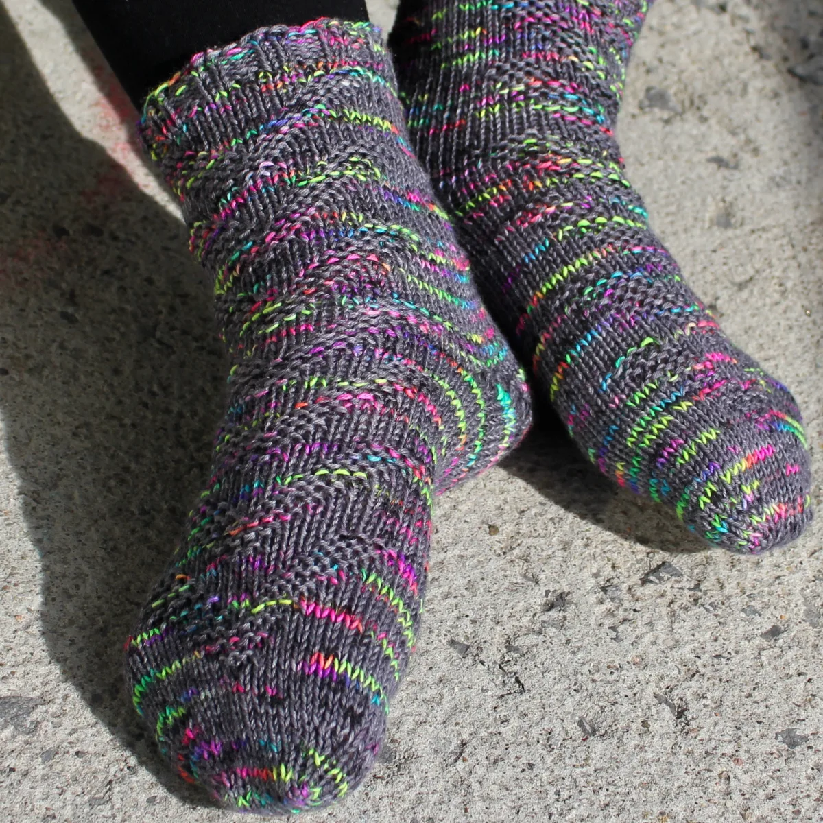 Feet wearing dark grey and rainbow socks with raised chevron texture.
