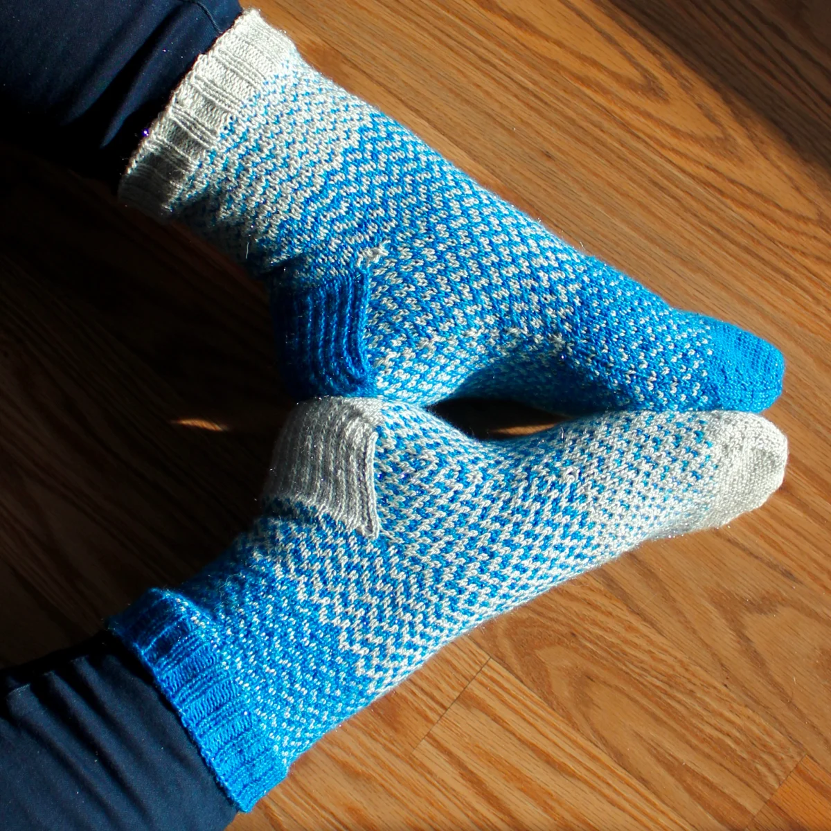 Feet heel-to-heel wearing fraternal blue and white sparkly colourwork socks.
