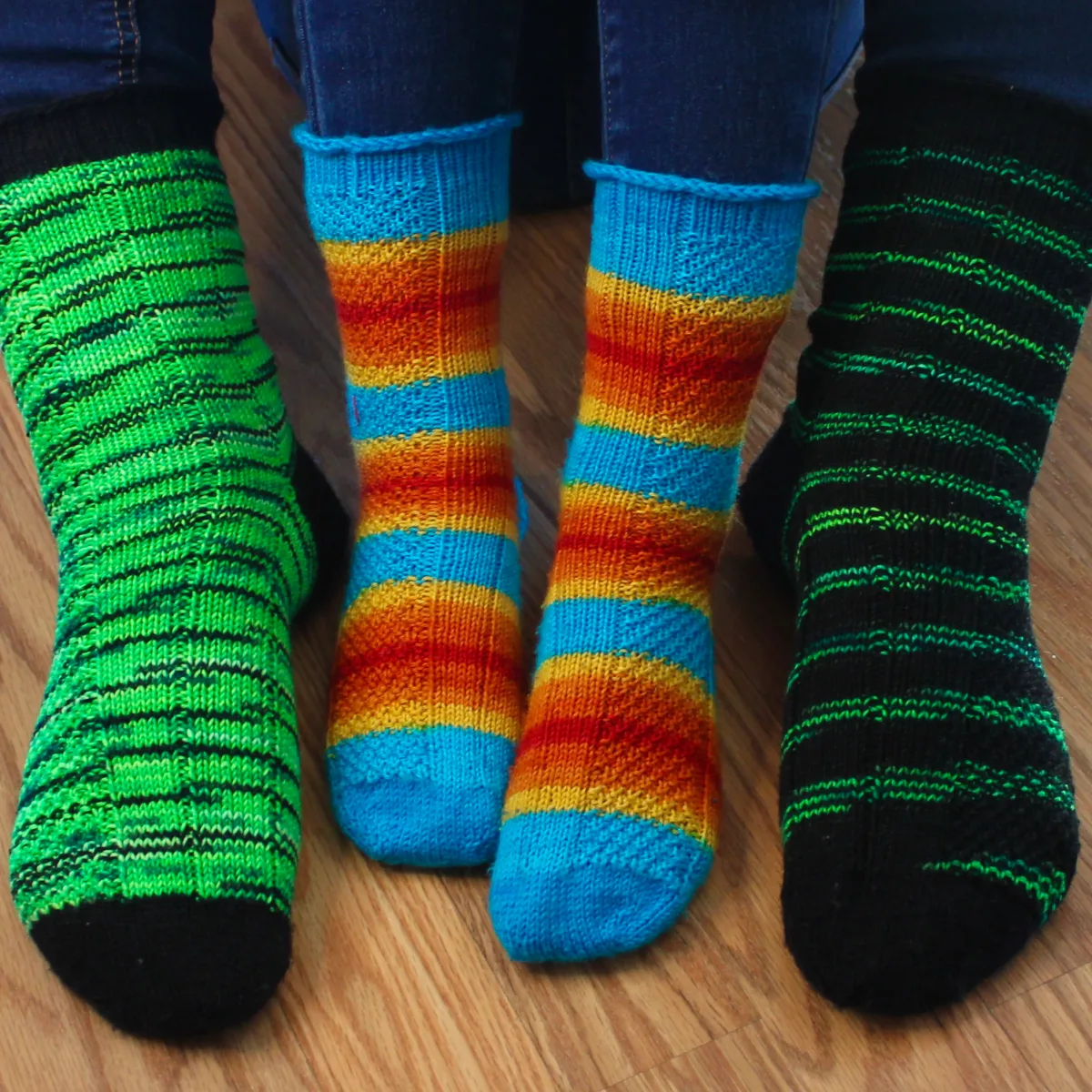 Small child feet wearing striped socks with texture detail between adult feet wearing green and black socks with the same texture detail.