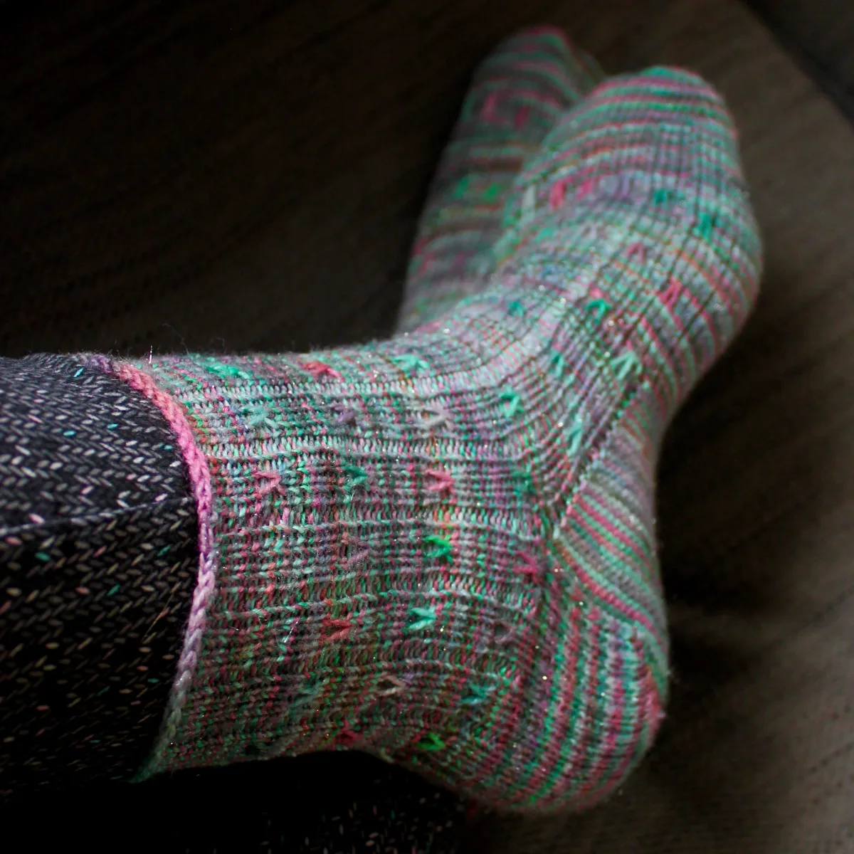 Crossed feet wearing green ribbed socks with coral and purple spiralling surface detail.