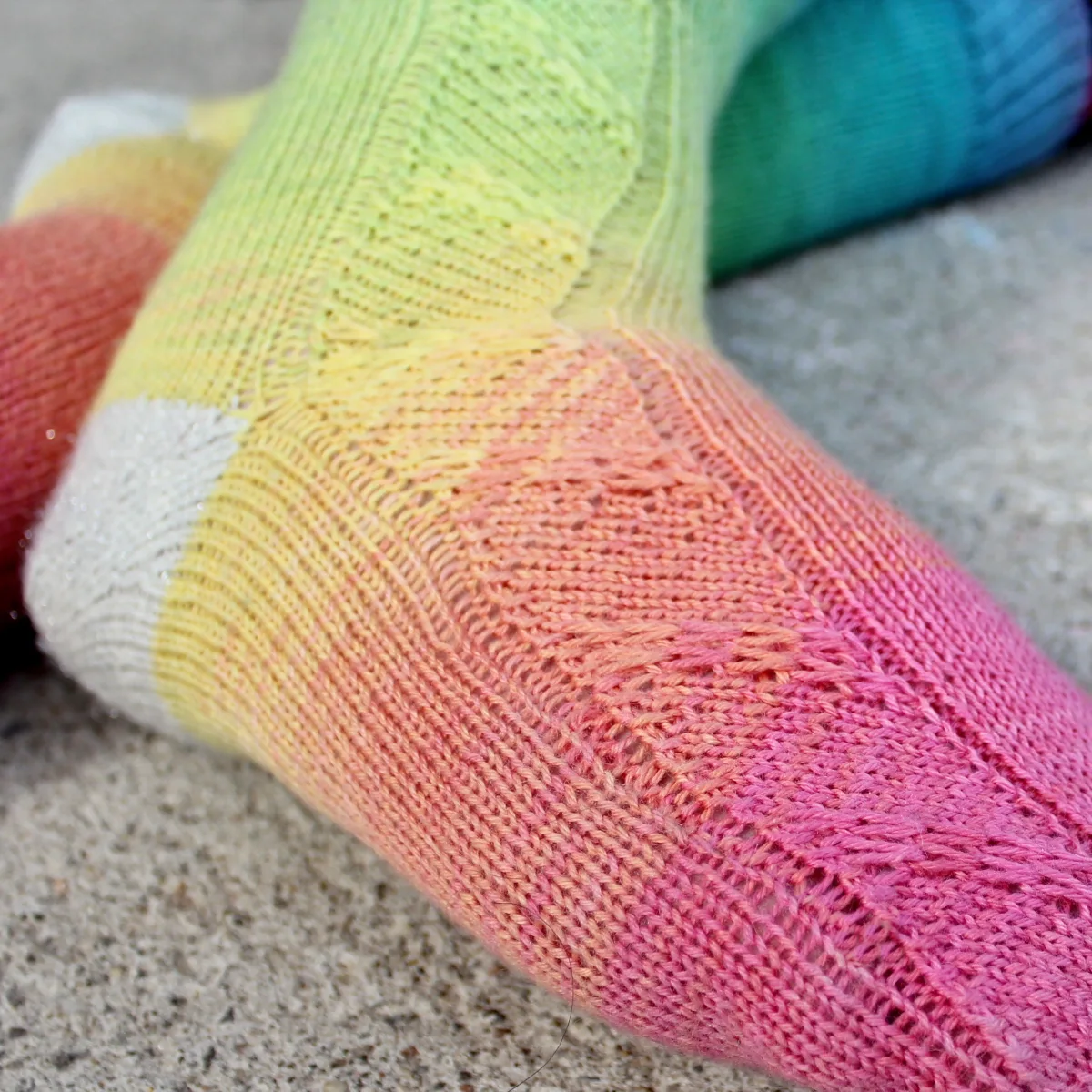 Closeup of feet wearing rainbow socks with diagonal slipped-stitch panel and sparkly white heels.