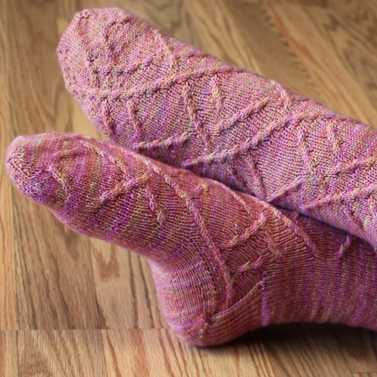 Close up of crossed feet wearing pink-orange socks with cabled surface detail.