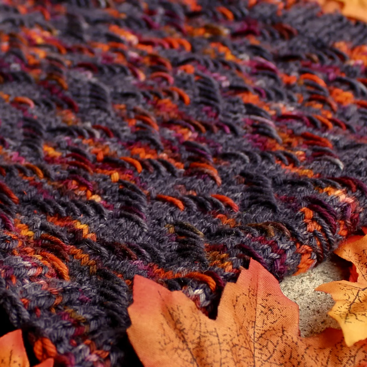 Close up of knitted cowl that is black with bright orange and burgundy highlights in a zigzag texture.