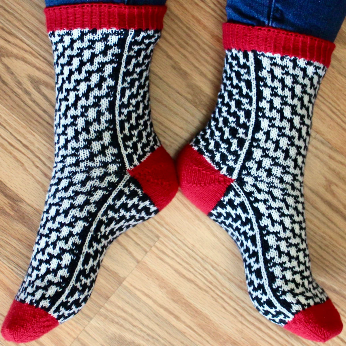 Side view of stranded colourwork socks with black and white mirrored and negative-image optical-illusion lines and red heels, toes, and cuffs.