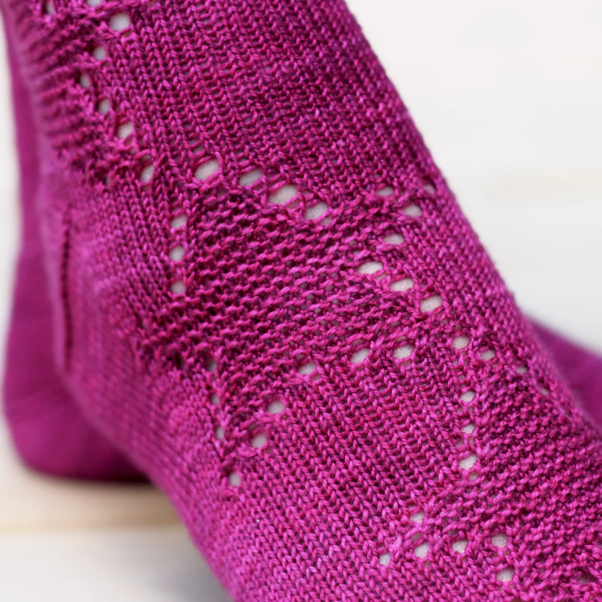 Close up of feet wearing dark pink knitted socks with star motif in texture and eyelets.