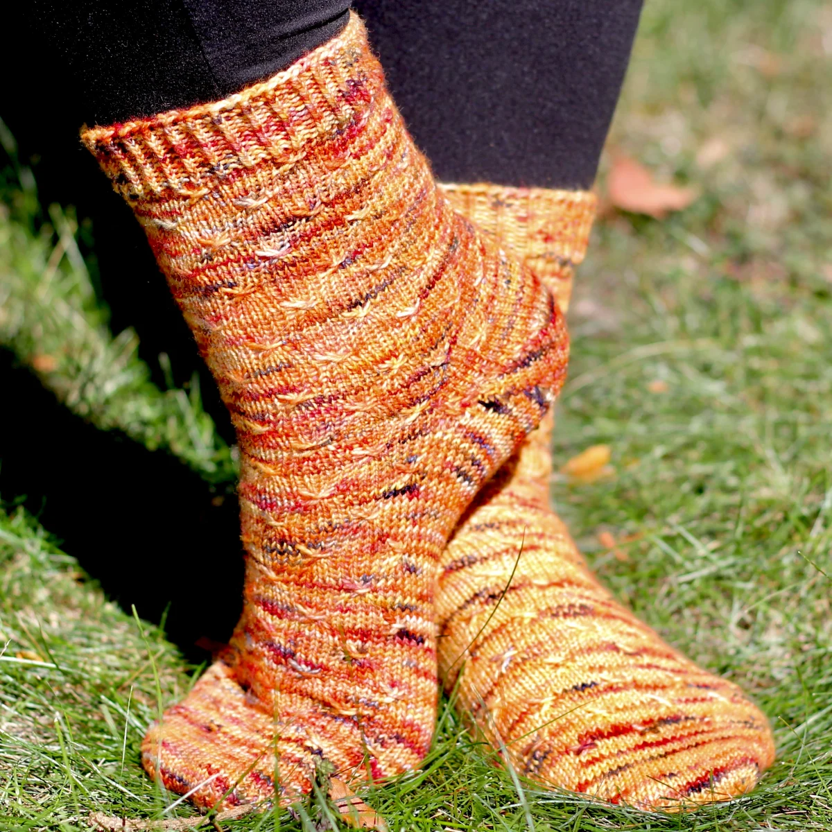 Side and front view of orange socks with asterix-like cable texture.