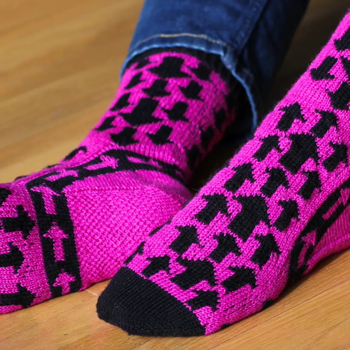 Feet wearing black and pink stranded colourwork socks with arrow motifs pointing down on the leg, up on the foot, and around the ankle.