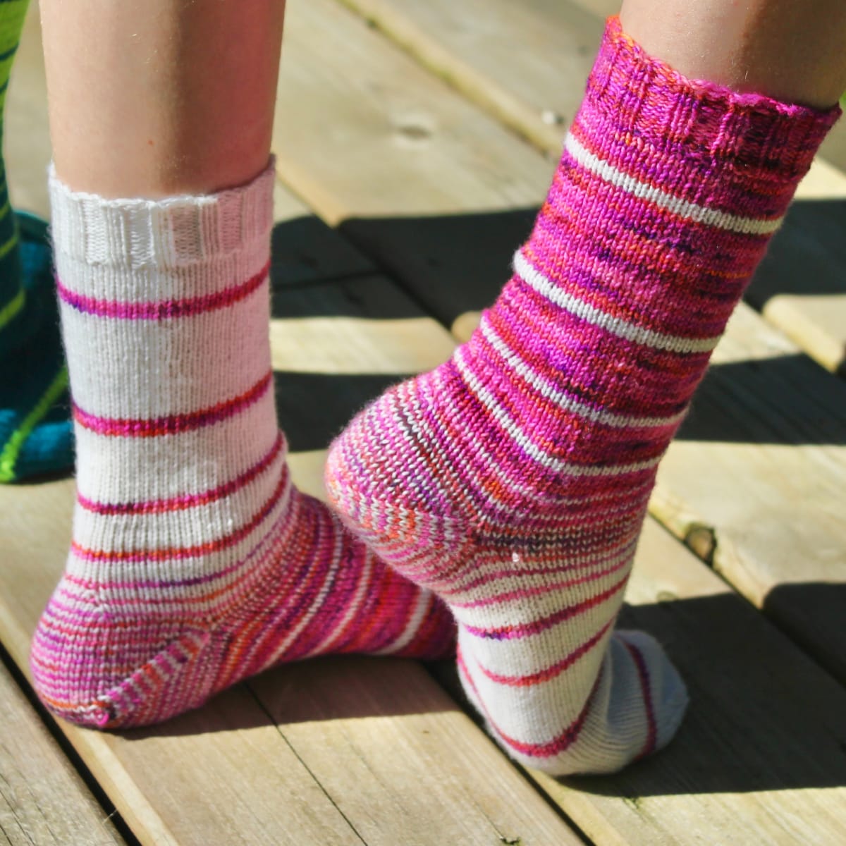 Feet wearing knitted socks with variable-width stripes that are made up of white and multicoloured pink, purple, and orange yarn.