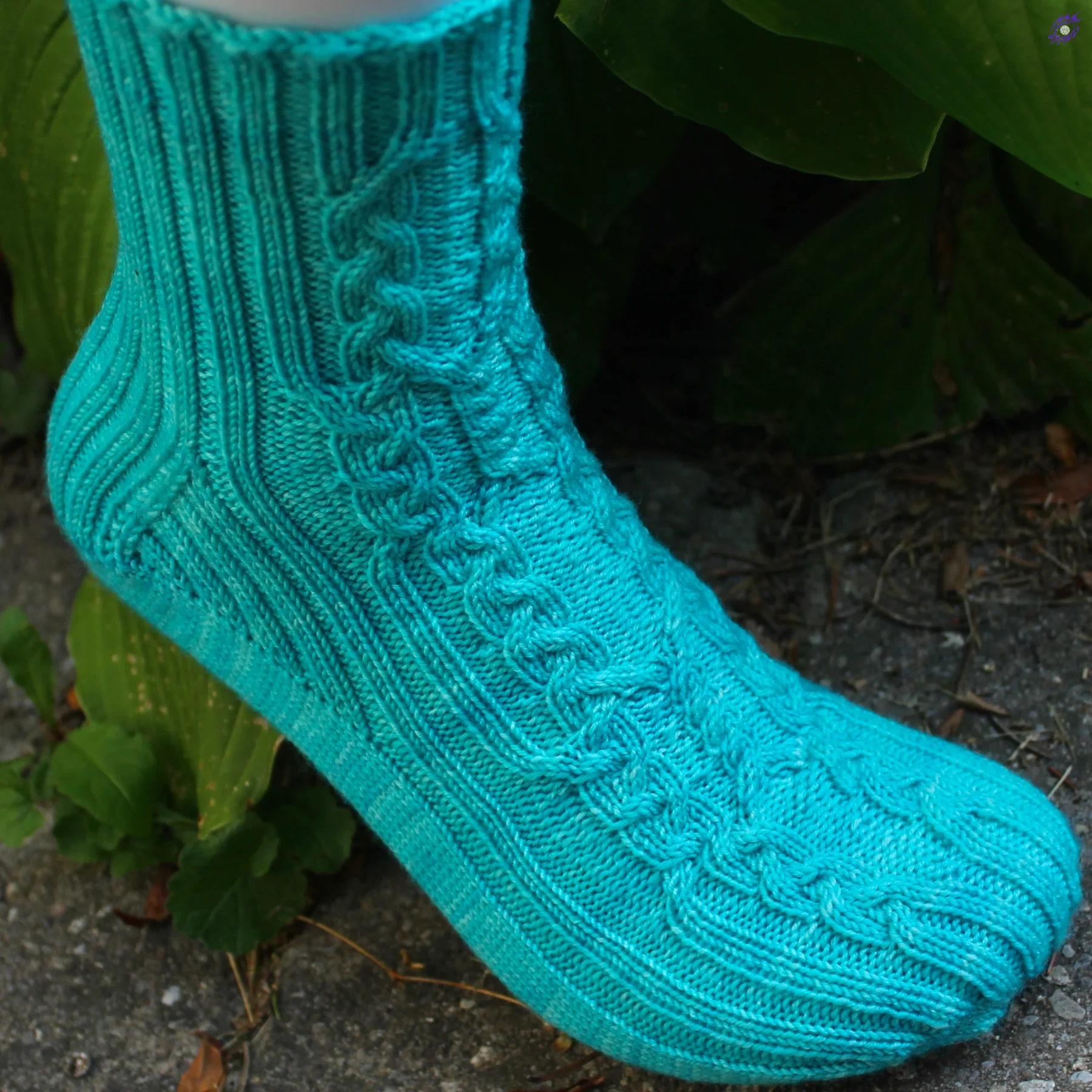 Foot wearing bright aqua knitted socks with intricate cable motif and ribbed accents.