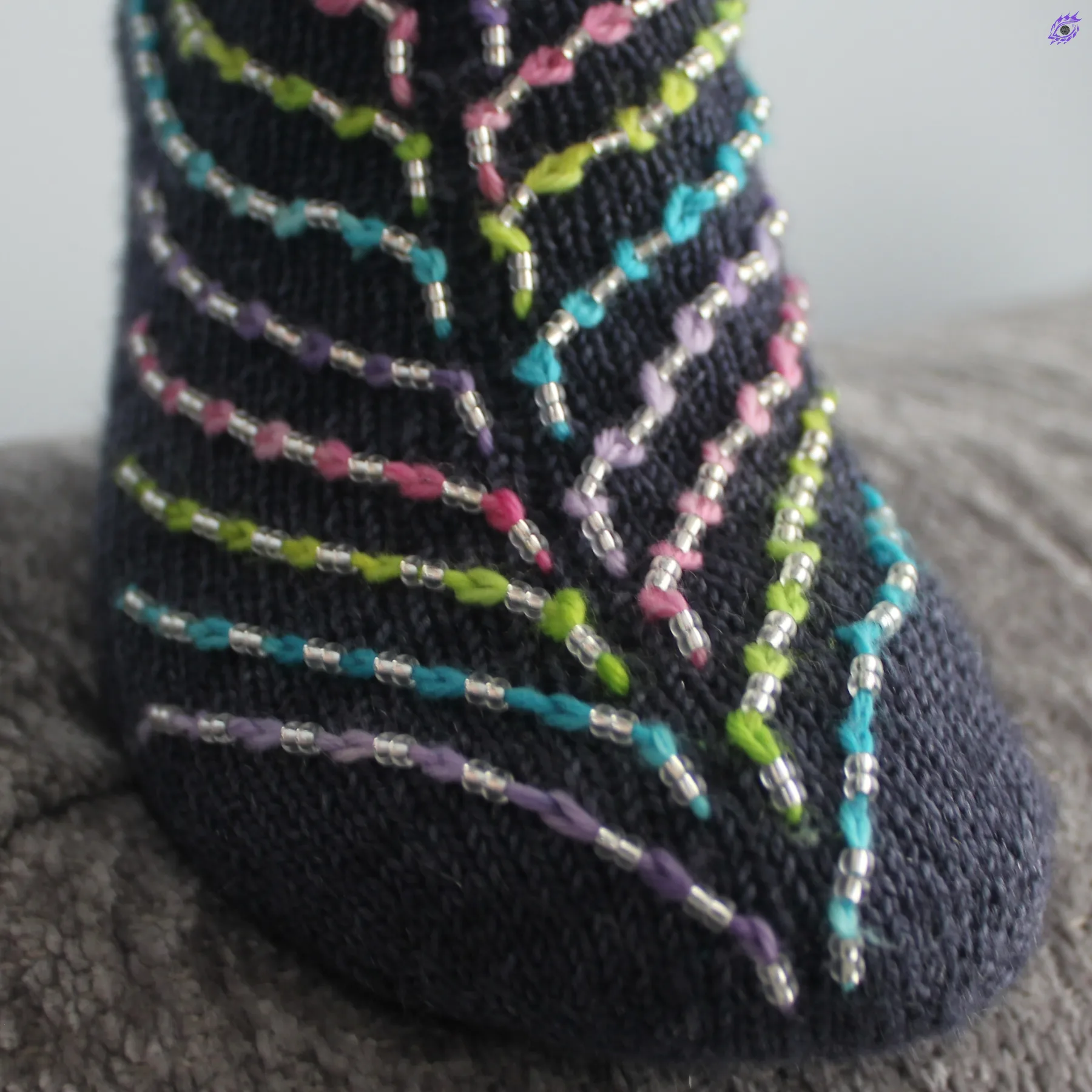 Close up of toe of dark blue socks with beads on diagonal strands of neon coloured contrast yarn.