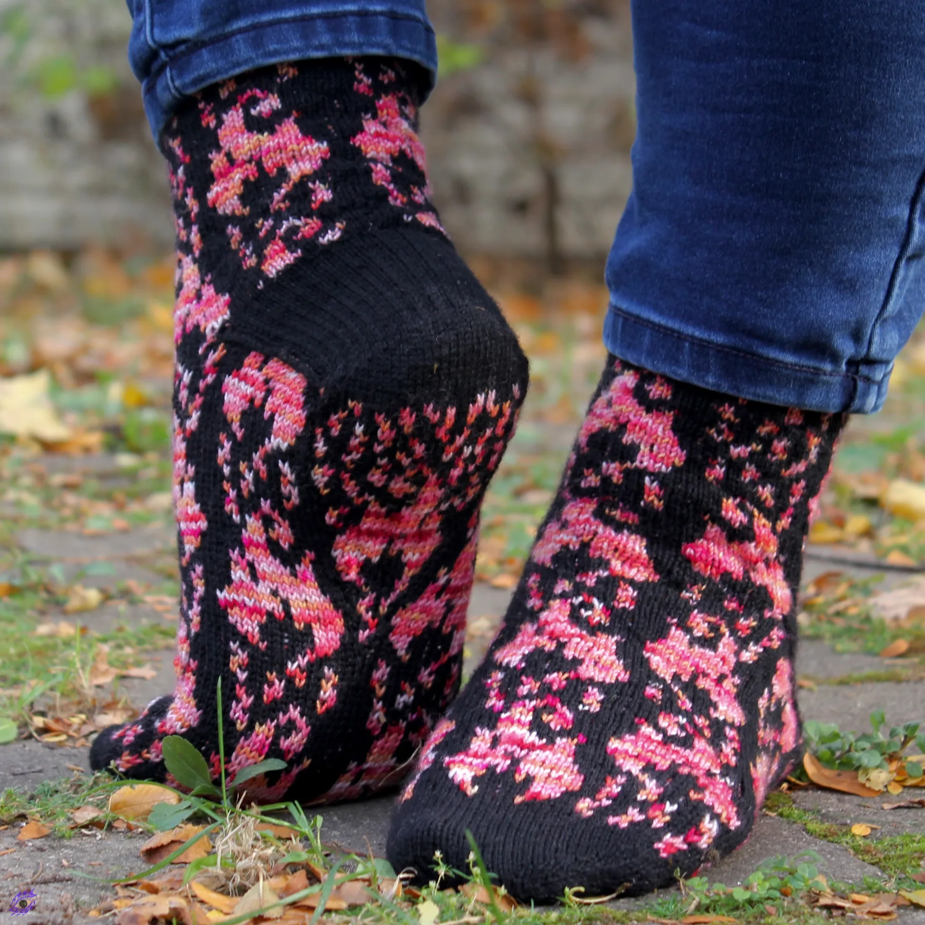 Feet wearing stranded colourwork socks with pink-orange flame motifs on a black background, with matching motif on the sole.