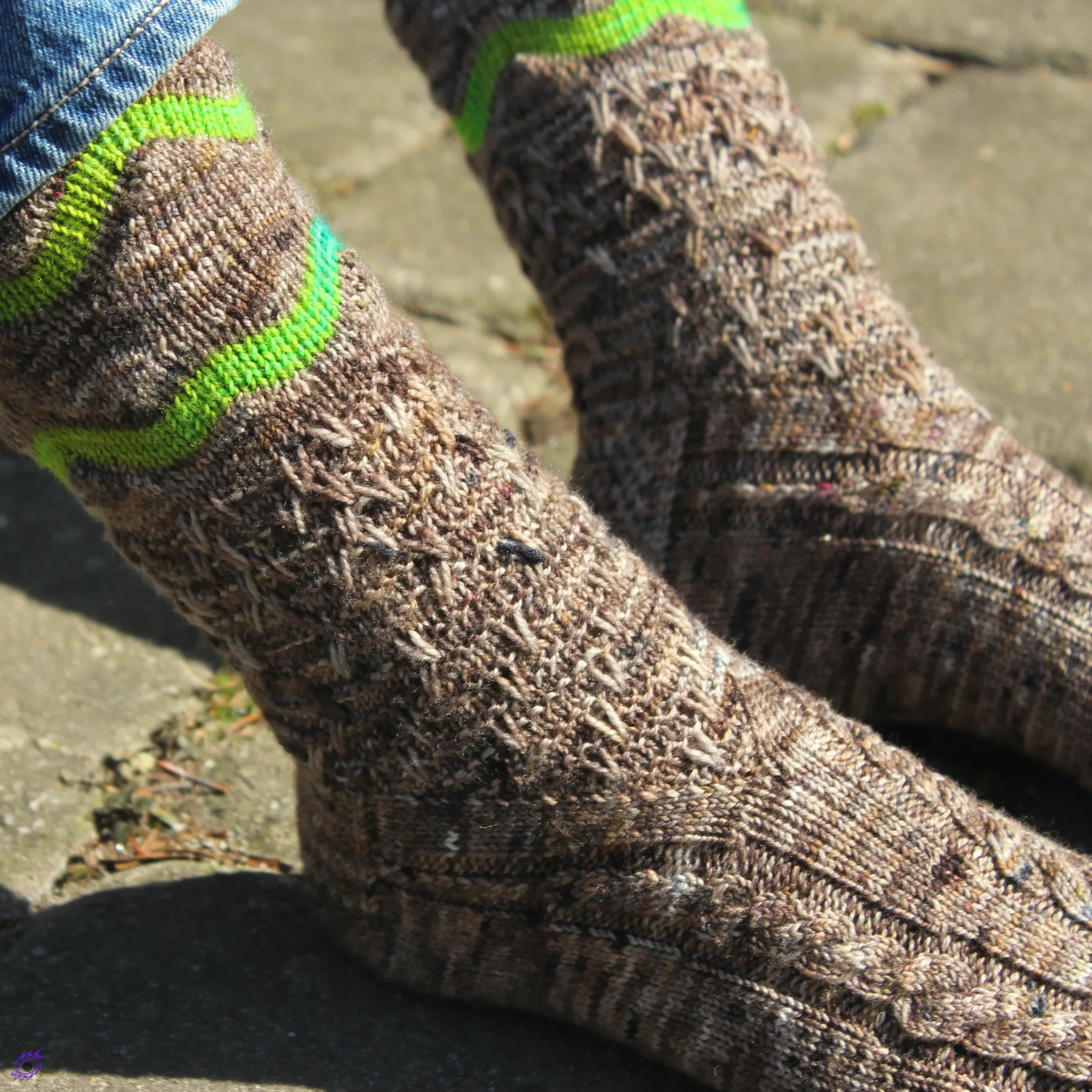 Feet wearing brown knitted socks with bright green accent and cable and texture details.