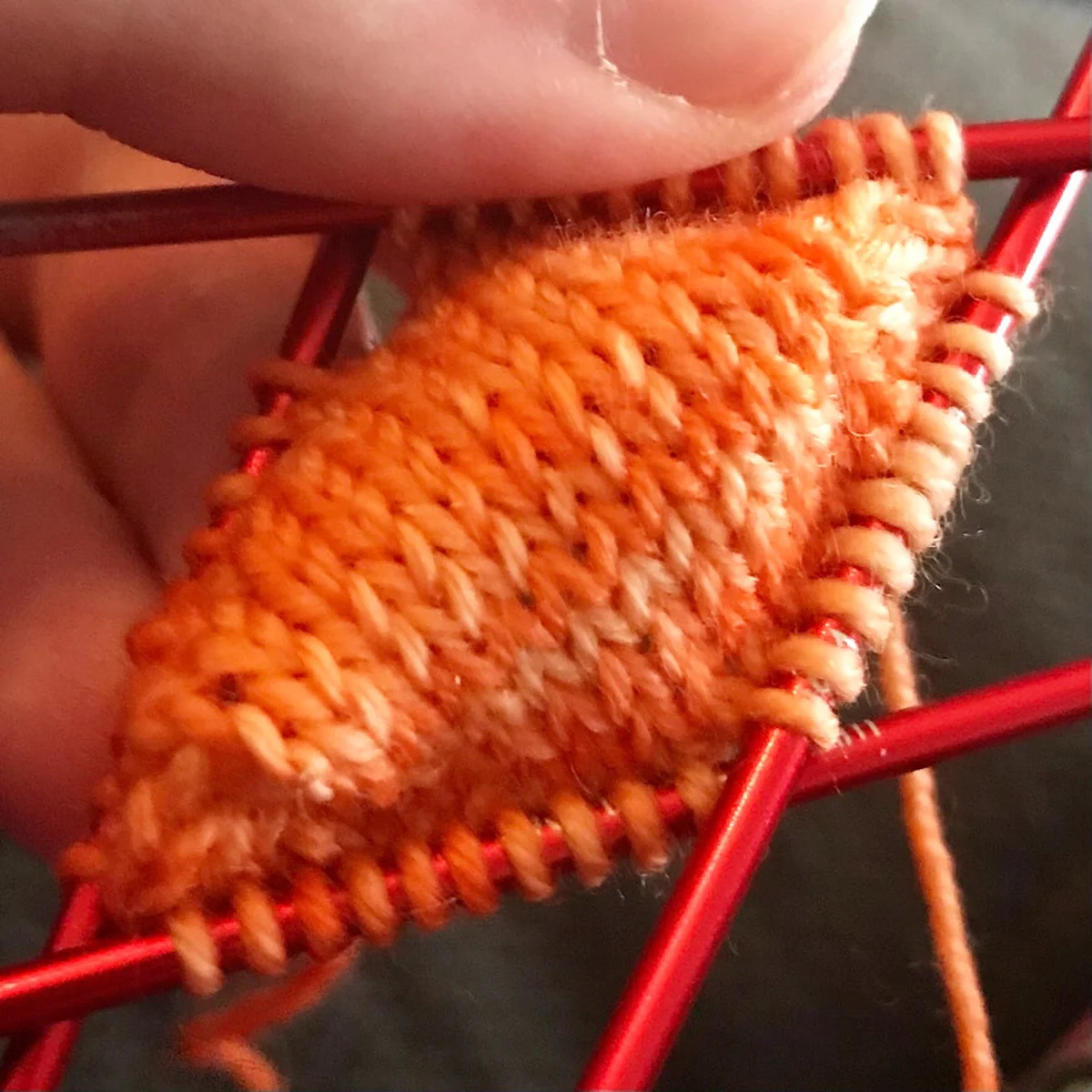 Tip of toe of orange knitted sock on double-pointed knitting needles.