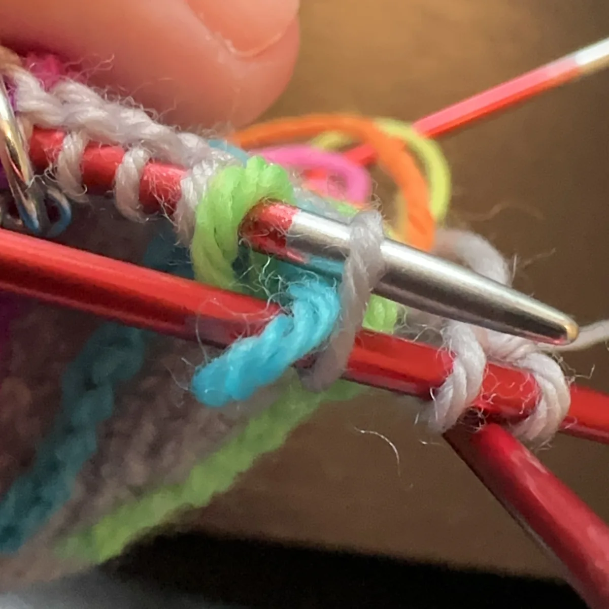 Hands holding knitted sock in progress; the needles are holding blue, green, and grey stitches.