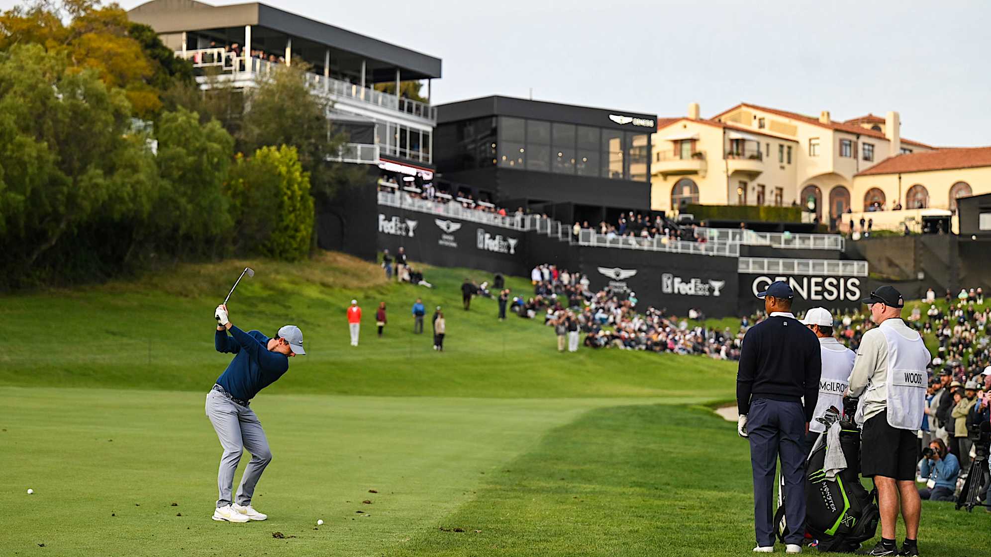 PACIFIC PALISADES, CA - FEBRUARY 16:  Rory McIlroy of Northern Ireland plays his shot from the 18th hole fairway as Tiger Woods looks on during the first round of the Genesis Invitational at Riviera Country Club on February 16, 2023 in Pacific Palisades, California. (Photo by Keyur Khamar/PGA TOUR via Getty Images)