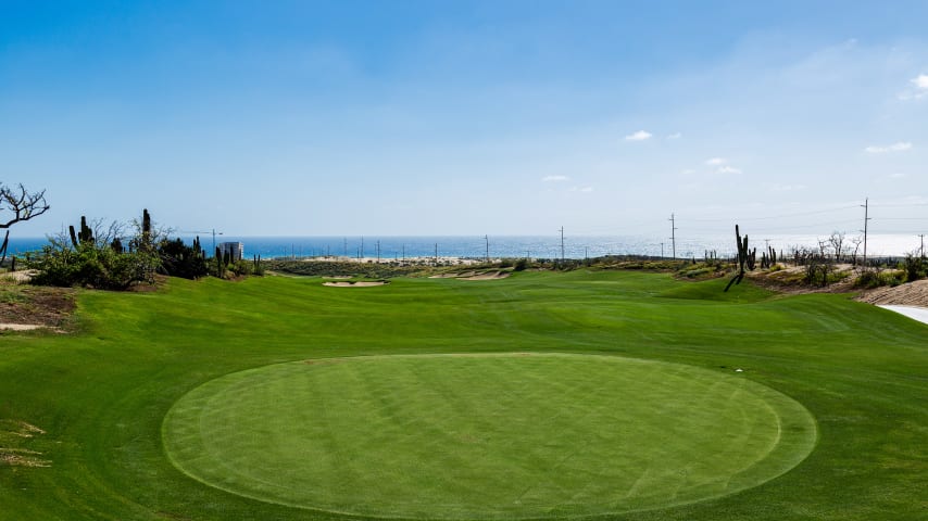 The opening hole is a mid-length par 5 that plays dramatically downhill into large sand dunes, offering panoramic views of the Pacific Ocean. On the tee shot, carrying the short left fairway bunker allows players to access a speed slot in the fairway, providing the shortest route to reach the green in two. There is ample fairway on the right side to avoid the bunker, but this angle requires a longer path to the green. The second landing area and green are nestled in a valley below the towering sand dunes. The surrounding slopes influence the ball's behavior around the green, introducing a recurring theme throughout the course, where players can use feeder slopes to navigate the putting surfaces.