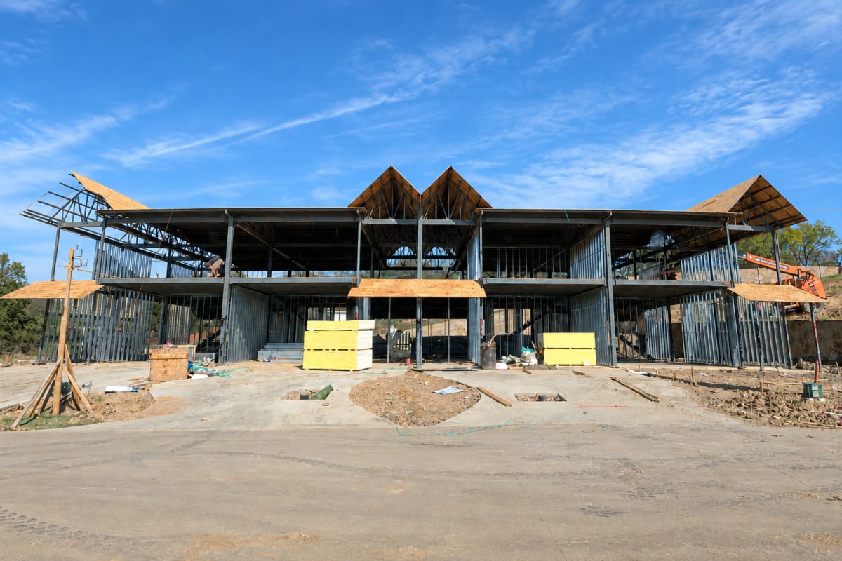 Red-iron structural steel frame of the Premier Parkway townhome collection during construction, showing the connected building's steel columns and roof trusses