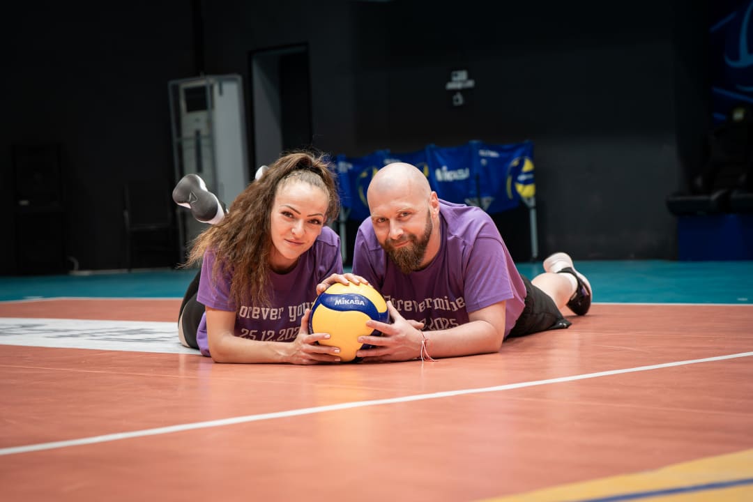 Couple in volleyball hall posing with ball on the ground