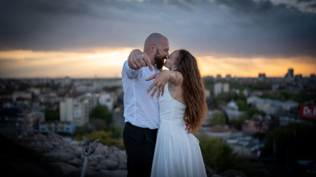 A man and a woman at sunset. The man shows off the engagement ring.