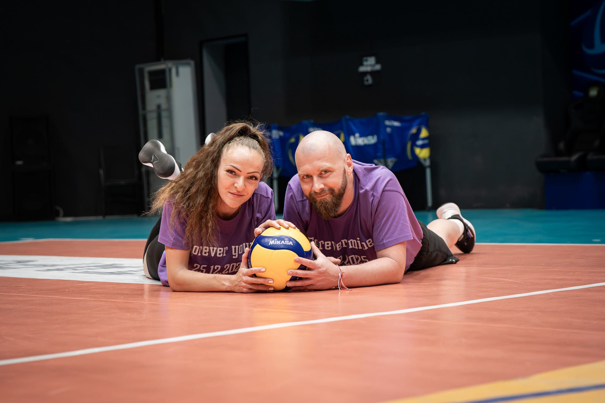 Couple in volleyball hall posing with ball on the ground