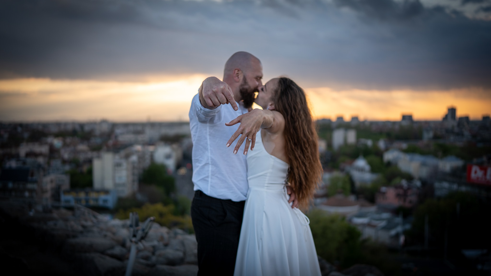A man and a woman at sunset. The man shows off the engagement ring.