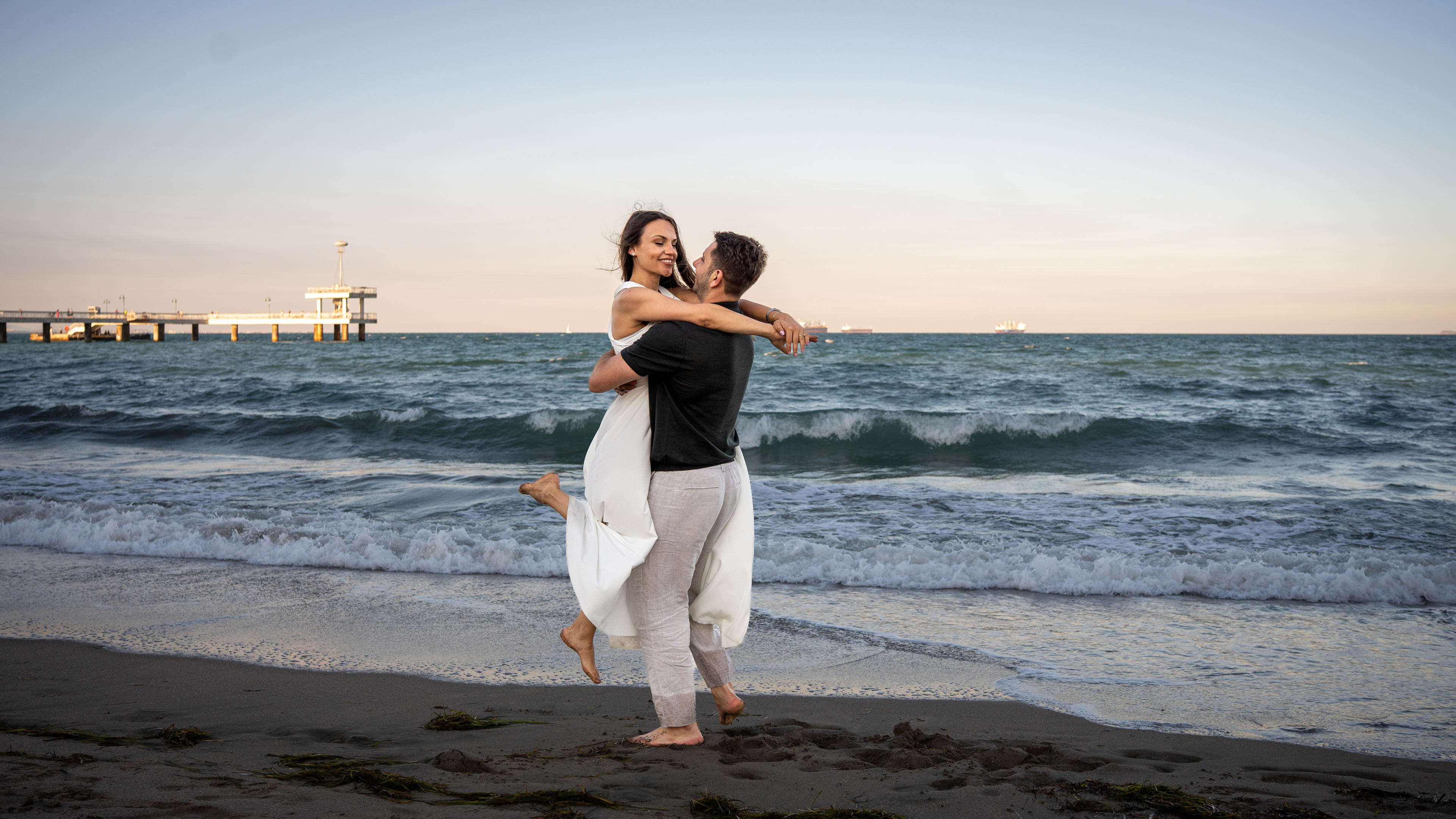 A young couple embracing by the sea, with waves in the background.