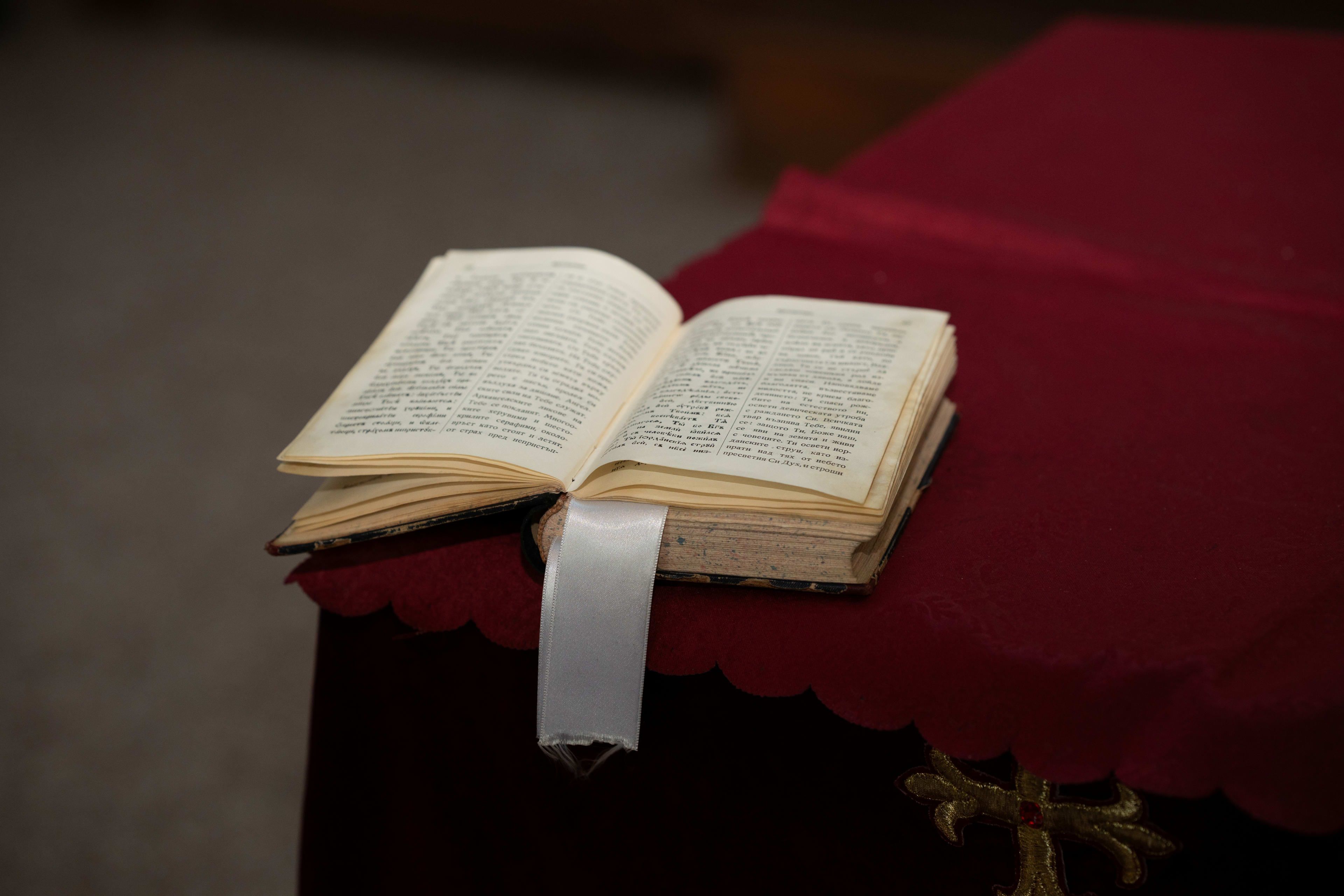 En åpen bibel som hviler på en rød dukoverflate. Et hvitt bånd markerer en side, og teksten er synlig.
