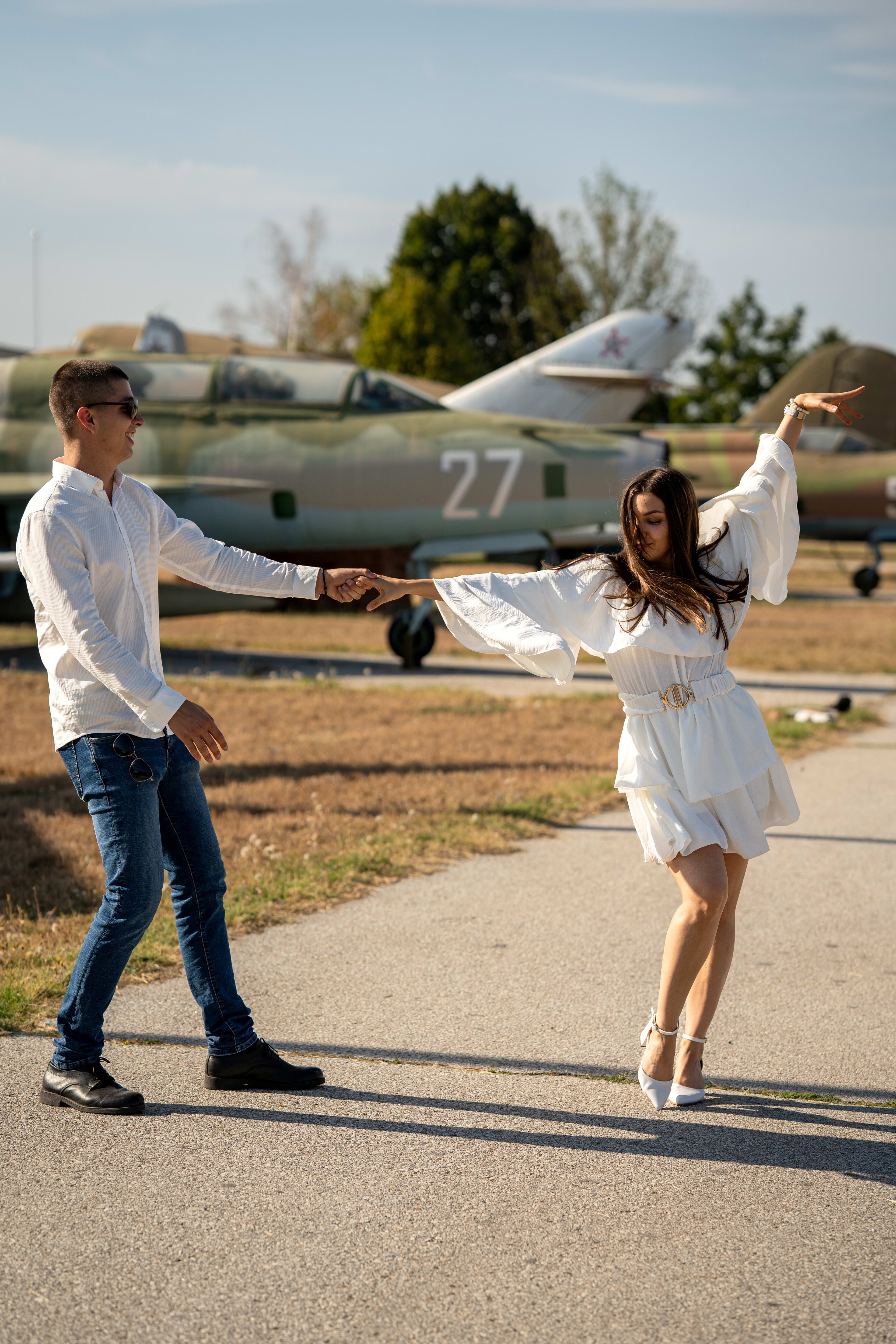 Couple dancing among airplanes. The woman is in a white dress, and the man is in a white shirt and jeans.