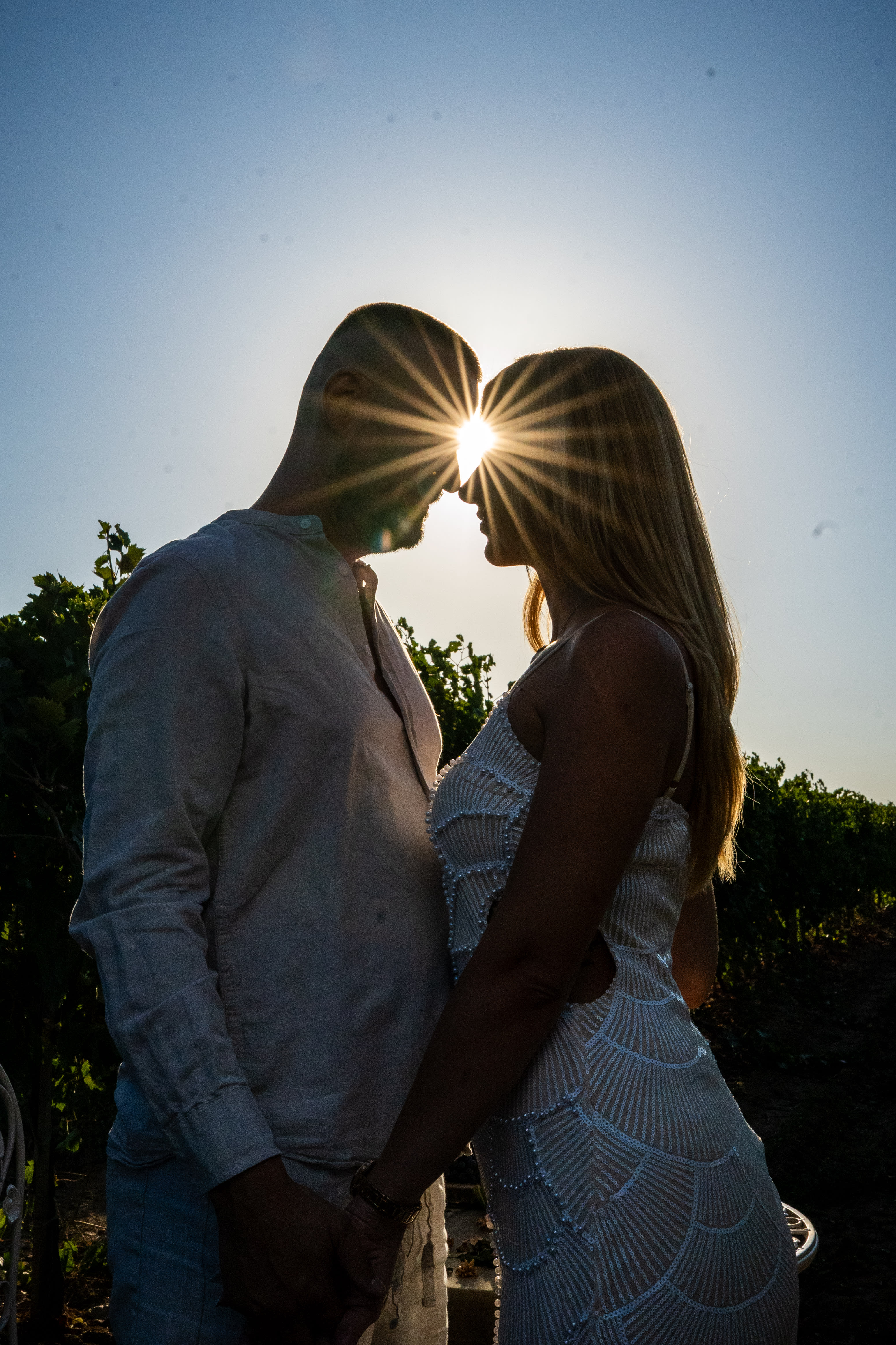 Couple looking lovingly at each other in the vineyards during sunset. Their foreheads are almost touching as the golden sunlight shines on them.