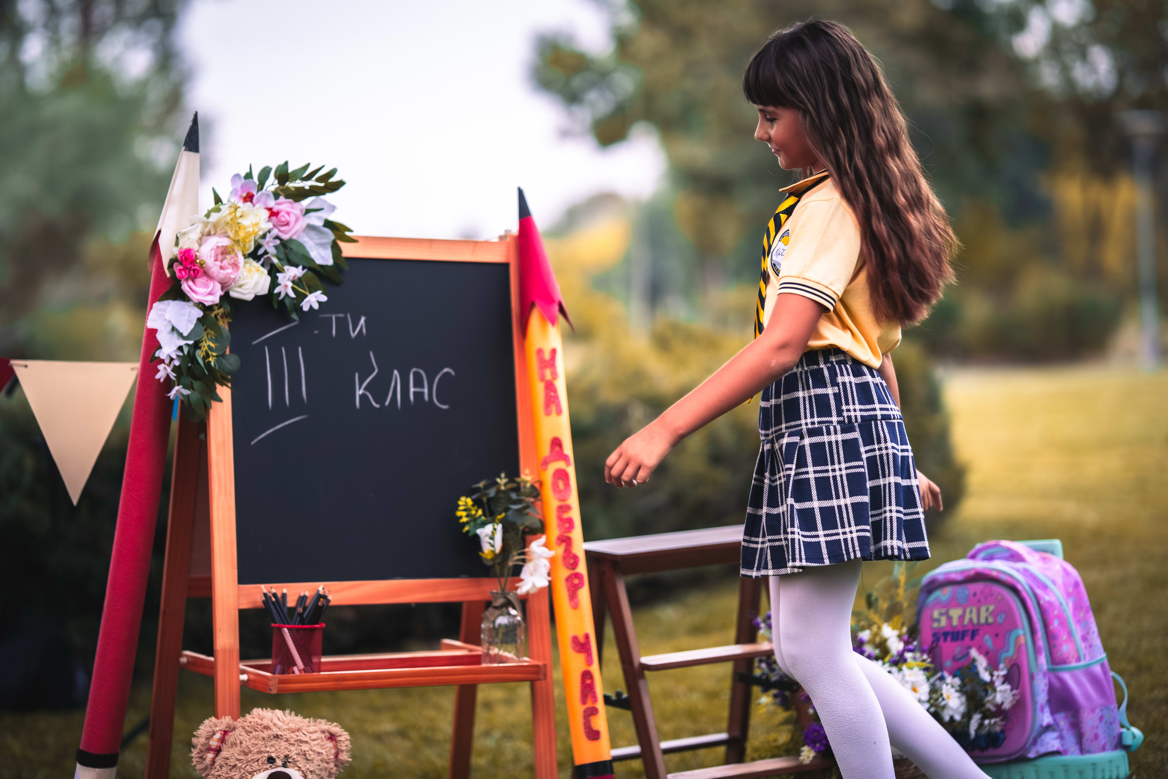 Schoolgirl in uniform posing in front of a school set with a chalkboard. She is approaching the board to write something.