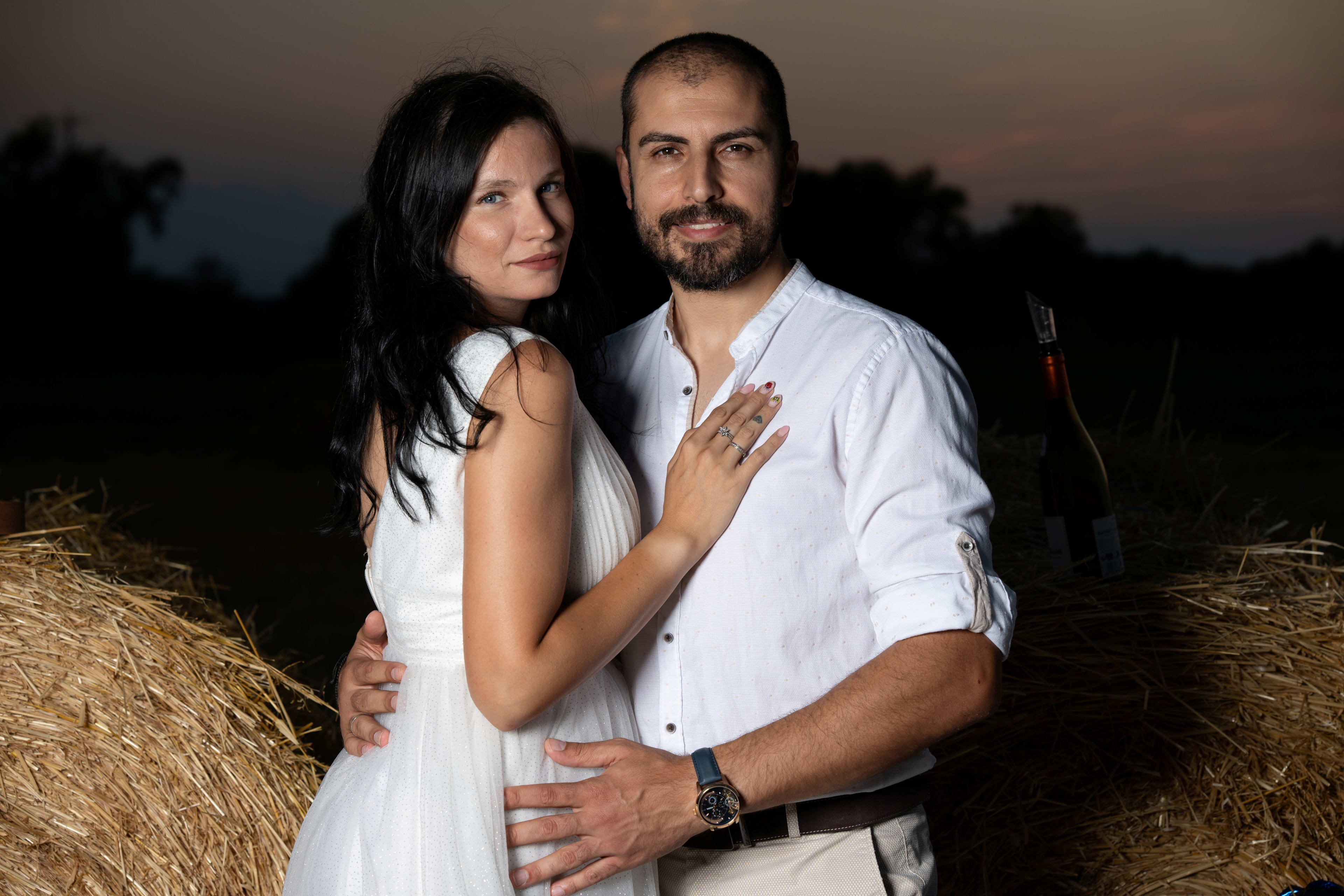 A man and woman embrace lovingly in a field of straw and straw bales.