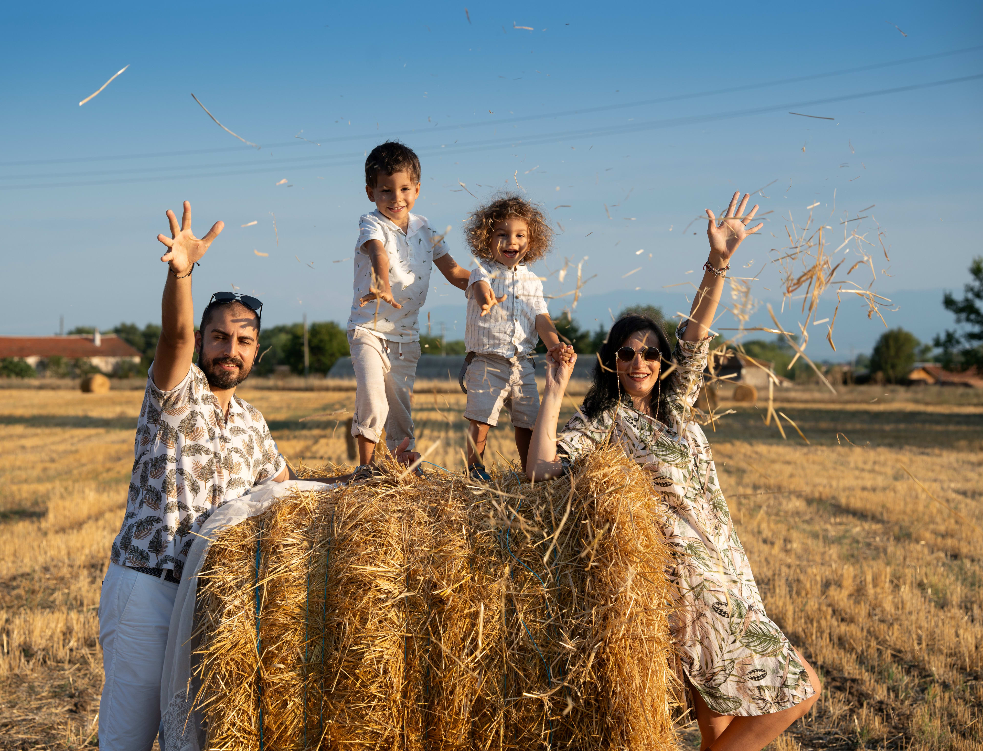Family on a straw bale throwing straw in the air and smiling.